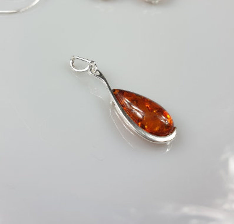 May include: A silver pendant with a teardrop-shaped amber stone.