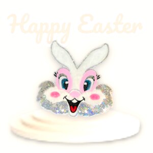 May include: White headband with a sparkly, pink-nosed bunny face. The bunny has blue eyes and a pink nose. The headband says "Happy Easter" in white text.