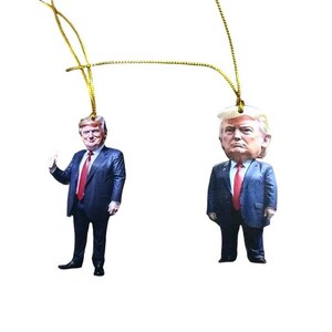 May include: Two Christmas ornaments featuring a caricature of a man in a blue suit and red tie. The ornaments are made of wood and have a gold string for hanging.