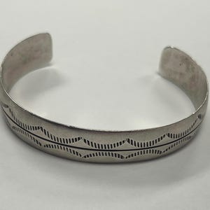 May include: A silver bracelet with a geometric design. The bracelet is made of a smooth metal and has a simple, elegant look.