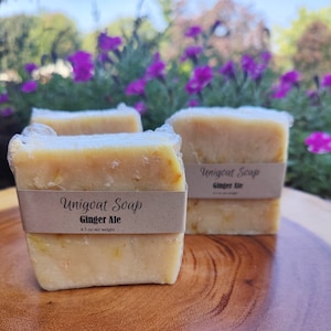 May include: Three bars of handmade soap wrapped in plastic. The soap is a light yellow color and has a label that reads "Unigoat Soap Ginger Ale 4.5 oz net weight".