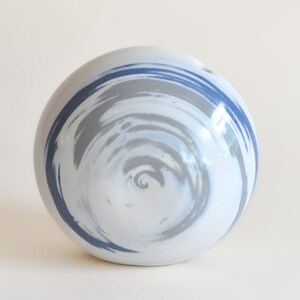 May include: A white ceramic vase with a swirling blue and gray pattern. The vase is round and has a small opening at the top.