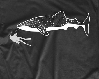 May include: A black t-shirt with a white silhouette of a whale shark and a scuba diver. The whale shark is swimming towards the diver.