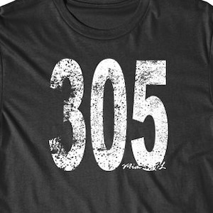 Puede incluir: Una camiseta negra con un gráfico blanco desgastado del número 305.