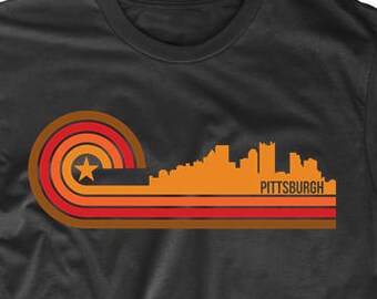 May include: A black t-shirt with a retro-style graphic of the Pittsburgh skyline in orange, red, and brown. The graphic features a star and the word "PITTSBURGH" in white.