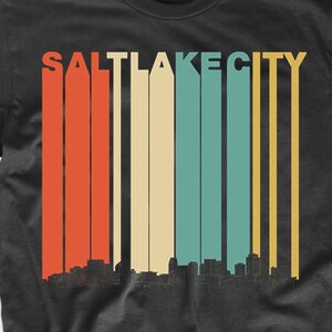 May include: Black t-shirt with a vintage-style graphic of the Salt Lake City skyline in red, orange, yellow, green, and blue.