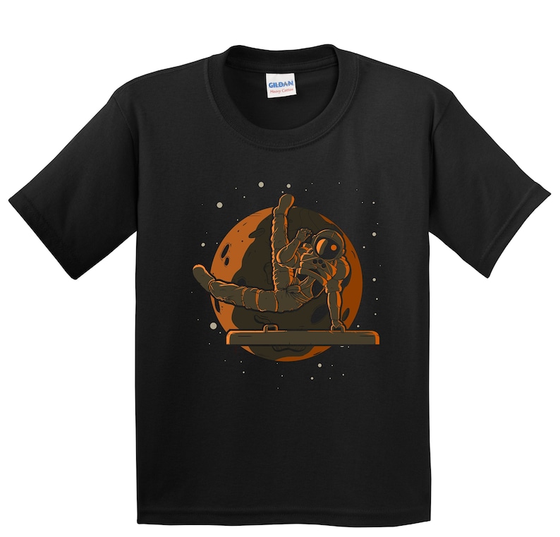May include: Black t-shirt with a graphic of an astronaut doing a handstand on a bar in front of a planet. The text "Gildan" is on the tag.