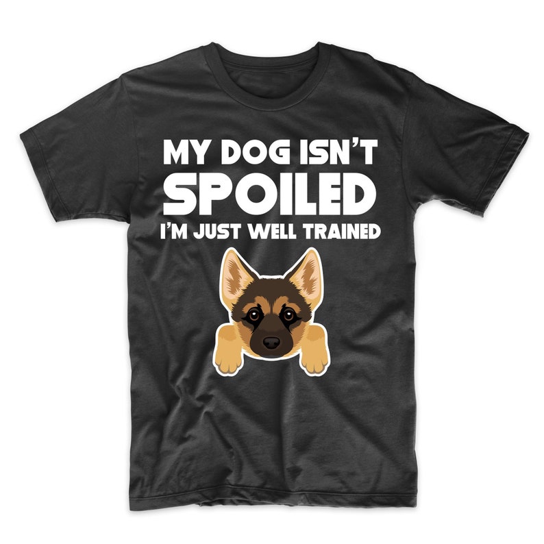 May include: Black t-shirt with the text "MY DOG ISN'T SPOILED I'M JUST WELL TRAINED" in white. A cartoon illustration of a German Shepherd dog is featured below the text. The dog has brown and black fur and is peeking over the bottom of the shirt.
