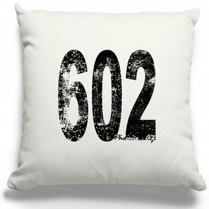 May include: White throw pillow with a black distressed graphic of the number 602. The text "Phoenix, AZ" is written in a smaller font below the number.