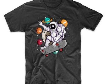 Puede incluir: Una camiseta gris oscuro con un gráfico de un astronauta patinando en el espacio. El astronauta lleva un traje espacial blanco y sostiene una patineta con ruedas rojas. Hay planetas y estrellas en el fondo.