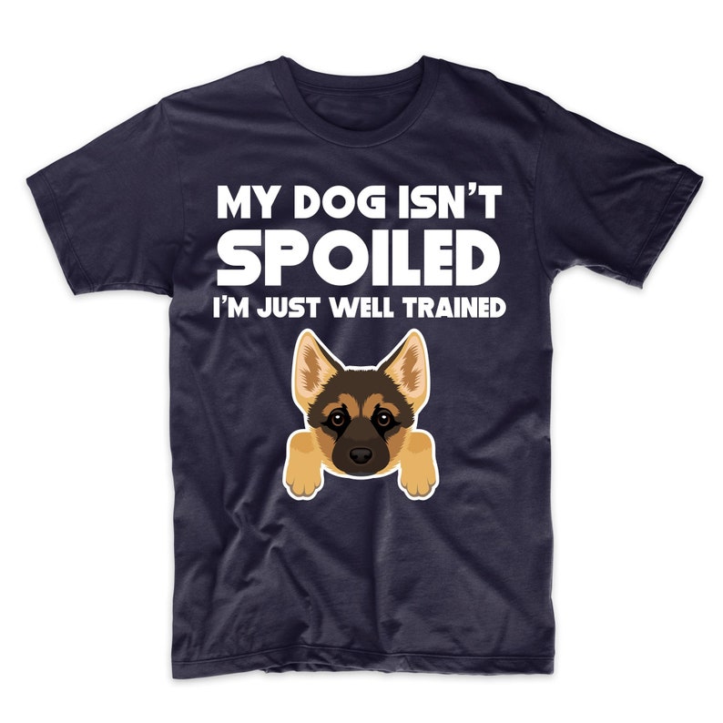 May include: Navy blue t-shirt with the text "MY DOG ISN'T SPOILED I'M JUST WELL TRAINED" in white. A cartoon German Shepherd dog graphic is featured below the text. The dog has tan and black fur and is peeking over the bottom of the shirt.