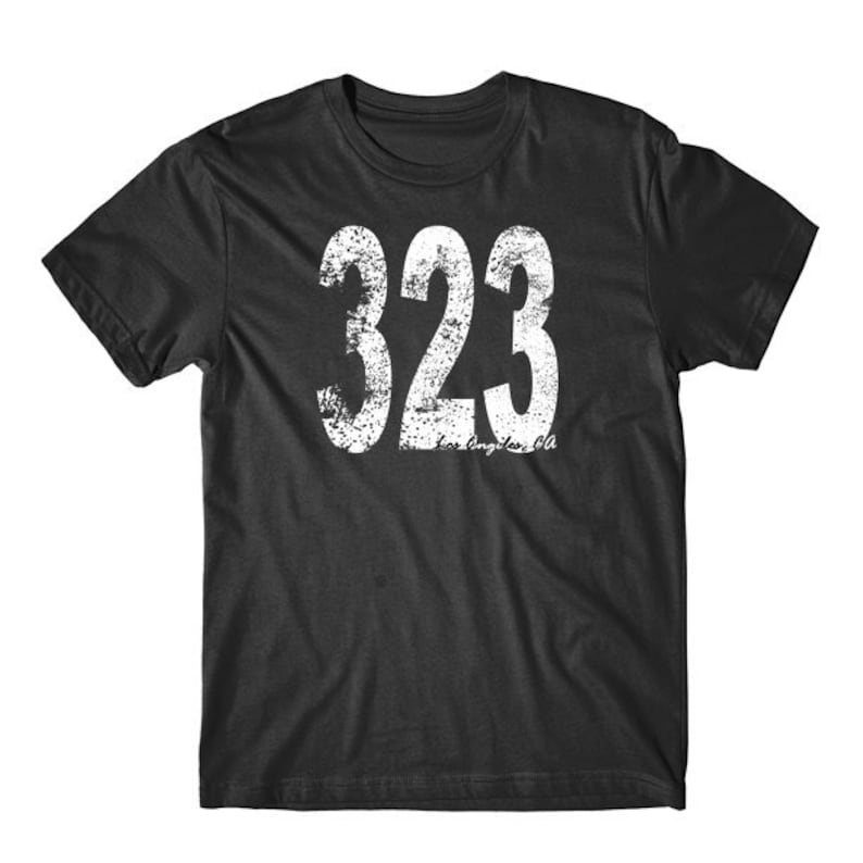 K&ouml;nnte beinhalten: Ein schwarzes T-Shirt mit einem wei&szlig;en, abgenutzten Aufdruck der Zahl 323 und dem Text "Los Angeles, CA".