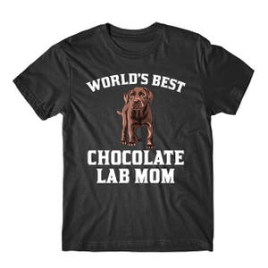 May include: A dark grey t-shirt with white text that reads "World's Best Chocolate Lab Mom". A brown Labrador Retriever puppy is pictured in the center of the shirt.