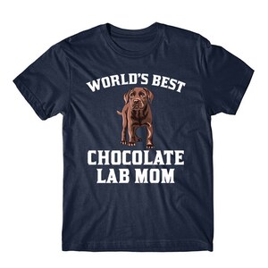 May include: A navy blue t-shirt with white text that reads "World's Best Chocolate Lab Mom". A brown Labrador Retriever puppy is pictured in the center of the shirt.