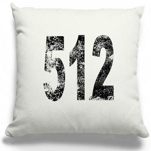 May include: Square, off-white throw pillow with the number "512" printed in distressed black font. The text "Austin, TX" is printed in a smaller font below the number. The pillow is likely made of a soft fabric.