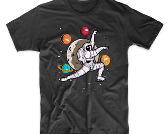 Puede incluir: Una camiseta negra con un gráfico de un astronauta patinando sobre hielo en el espacio. El astronauta lleva un traje espacial blanco y sostiene una pelota roja. Hay planetas y estrellas en el fondo.