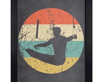 May include: A framed wall art print featuring a dark silhouette of a gymnast performing on rings. The figure is centered against a circular background divided into horizontal stripes of orange, white, light blue, and yellow with a distressed texture.