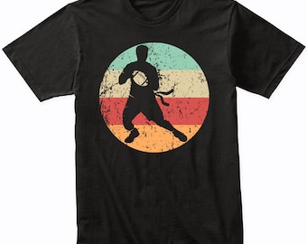 May include: A black t-shirt featuring a vintage-style graphic of a person playing American football. The graphic is in a circle with a red, orange and blue colour scheme.