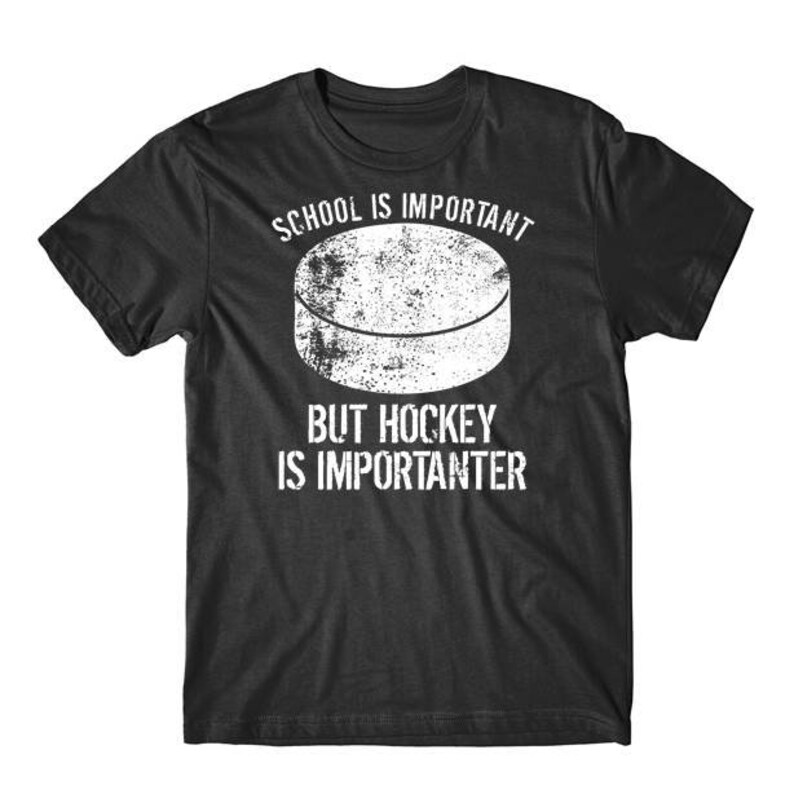 Op de afbeelding: Zwart T-shirt met witte tekst die luidt "School is belangrijk, maar hockey is belangrijker". Boven de tekst staat een witte afbeelding van een hockeypuck.