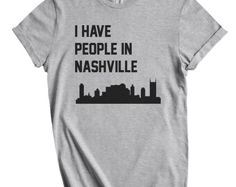 Puede incluir: Camiseta gris claro con mangas enrolladas. La camiseta presenta el texto "I HAVE PEOPLE IN NASHVILLE" sobre una silueta negra del horizonte de Nashville.