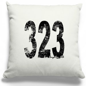 May include: White throw pillow with black distressed lettering that reads "323 Los Angeles, CA".