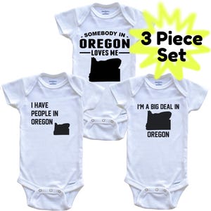 May include: Three white baby onesies with black text and a black Oregon state outline. The onesies read: "Somebody in Oregon Loves Me," "I Have People in Oregon," and "I'm a Big Deal in Oregon." A yellow burst graphic says "3 Piece Set."