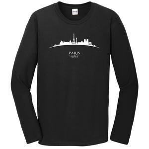 Op de afbeelding: Zwart T-shirt met lange mouwen met een wit silhouet van de skyline van Parijs, inclusief de Eiffeltoren, en de tekst "PARIS FRANCE".