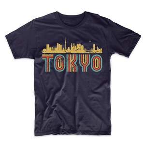 May include: A navy blue t-shirt with a vintage-style graphic of the Tokyo skyline and the word "TOKYO" in colorful, striped letters.
