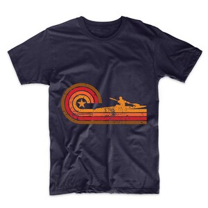 May include: A navy blue t-shirt with a retro-style graphic of a person kayaking in a sunset. The graphic features a red, orange, and yellow color scheme with a white star.