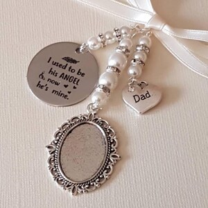 May include: A memorial charm featuring a round silver disc engraved with the text I used to be his ANGEL & now he's mine, a heart-shaped charm engraved with Dad, and an oval filigree frame, all accented with white faux pearls and a white ribbon.