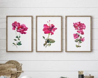 May include: Three framed watercolor paintings of pink hibiscus flowers with green leaves on a white wood wall above a white cabinet with two drawers and two doors.