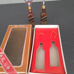 May include: A brown box with a red ribbon and the text "Bar Set" on it. The box contains two silver bottle openers, one with a corkscrew and one with a bottle opener. The box is open and the openers are visible.