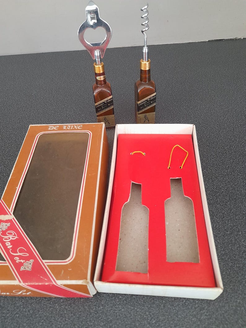 May include: A brown box with a red ribbon and the text "Bar Set" on it. The box contains two silver bottle openers, one with a corkscrew and one with a bottle opener. The box is open and the openers are visible.