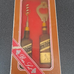 May include: A brown box with a red ribbon and the words "Bar Set" printed on it. The box contains two miniature bottles of Johnnie Walker scotch whiskey and a bottle opener and corkscrew.