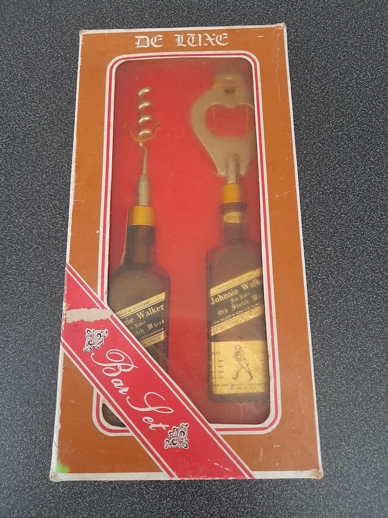 May include: A brown box with a red ribbon and the words "Bar Set" printed on it. The box contains two miniature bottles of Johnnie Walker scotch whiskey and a bottle opener and corkscrew.