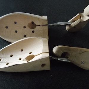 May include: Two wooden shoe trees with adjustable metal arms. The shoe trees are designed to help maintain the shape of shoes and prevent creases.