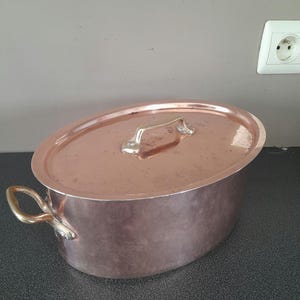 May include: A large oval copper pot with a lid and brass handles. The pot has a hammered finish and is in good condition.