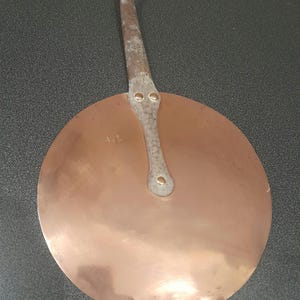 May include: A round copper pan with a long, thin handle. The handle has a loop at the top and is attached to the pan with two rivets. The pan is marked with the initials "A.L."
