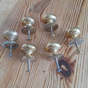May include: A collection of seven vintage brass door knobs with a rounded top and a circular base. The knobs are arranged on a wooden surface with visible wood grain.