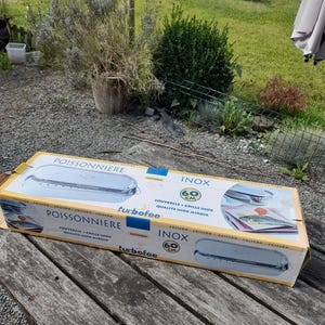 Puede incluir: Una caja de cartón para una pescadora de acero inoxidable turbofee, con el texto "POISSONNIERE" e "INOX 60 cm". La caja presenta imágenes de la pescadora y texto en francés. La caja está sobre una mesa de madera desgastada.