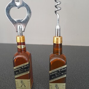 May include: Two miniature Johnnie Walker Old Scotch Whisky bottles with bottle opener and corkscrew tops. The bottles are brown glass with gold labels and black text.