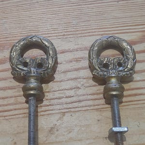 Peut inclure: Deux boutons de tiroir anciens en laiton. Chaque bouton présente un motif de couronne décorative avec une poignée en boucle. Les boutons ont des tiges filetées avec des écrous pour un montage sûr. La quincaillerie est probablement pour une armoire ou un tiroir.