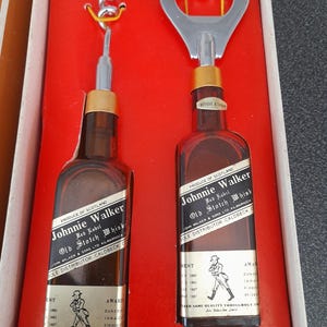 May include: A set of two miniature Johnnie Walker Red Label Scotch Whisky bottles with a bottle opener and corkscrew. The bottles are in a red box with the Johnnie Walker logo and text. The box also has a gold trim.