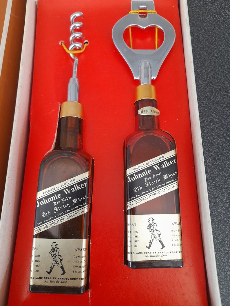 May include: A set of two miniature Johnnie Walker Red Label Scotch Whisky bottles with a bottle opener and corkscrew. The bottles are in a red box with the Johnnie Walker logo and text. The box also has a gold trim.