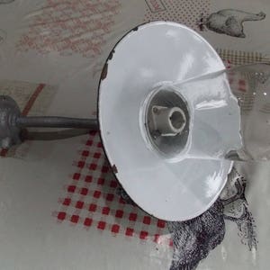May include: A white enamel outdoor wall light fixture with a clear glass globe and a metal arm. The light fixture is mounted on a wall and has a white enamel shade.