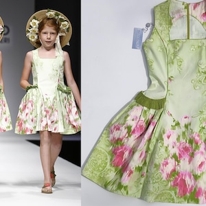 Peut inclure: Deux filles portant des robes vert clair à motifs floraux roses, défilant sur un podium. Les robes ont des encolures carrées et des volants. Elles sont accessoirisées de chapeaux de paille ornés de fleurs.