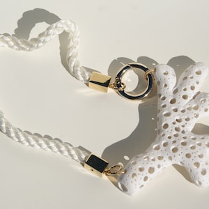 K&ouml;nnte beinhalten: Wei&szlig;e Seilkette mit goldenem Verschluss und wei&szlig;em korallenf&ouml;rmigem Anh&auml;nger. Die Kette hat ein geflochtenes Seildesign und einen goldfarbenen Verschluss. Der Korallenanh&auml;nger hat eine por&ouml;se Textur.
