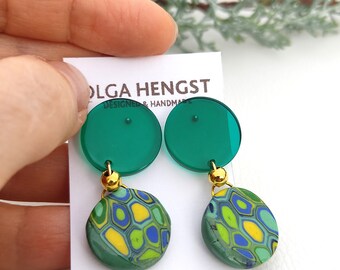 May include: A pair of green and yellow patterned earrings with gold accents. The earrings are made of polymer clay and have a round shape. The earrings are hanging from a green disc.