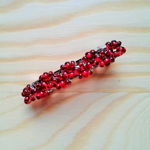 May include: A red beaded hair clip with a silver metal base.