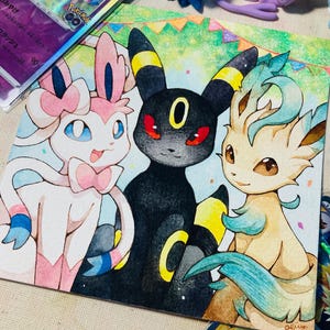 K&ouml;nnte beinhalten: Aquarellillustration von drei Pok&eacute;mon-Charakteren: Sylveon, Umbreon und Leafeon. Sylveon ist rosa und wei&szlig;, Umbreon ist schwarz mit gelben Akzenten und Leafeon ist hellbraun und gr&uuml;n. Pok&eacute;mon-Sammelkarten und Figuren umgeben das Kunstwerk.
